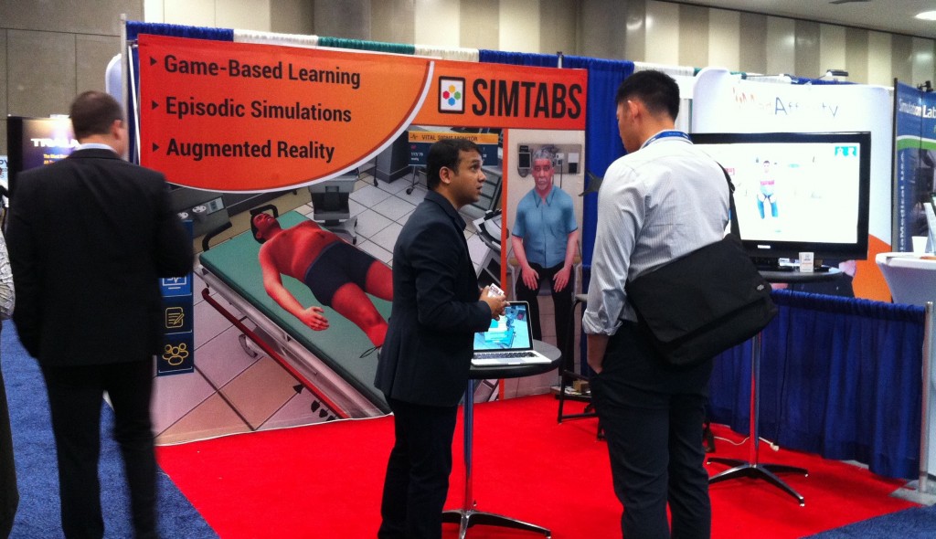 Photo of SimTabs booth with a large pictorial backdrop, and computer displays on tables.